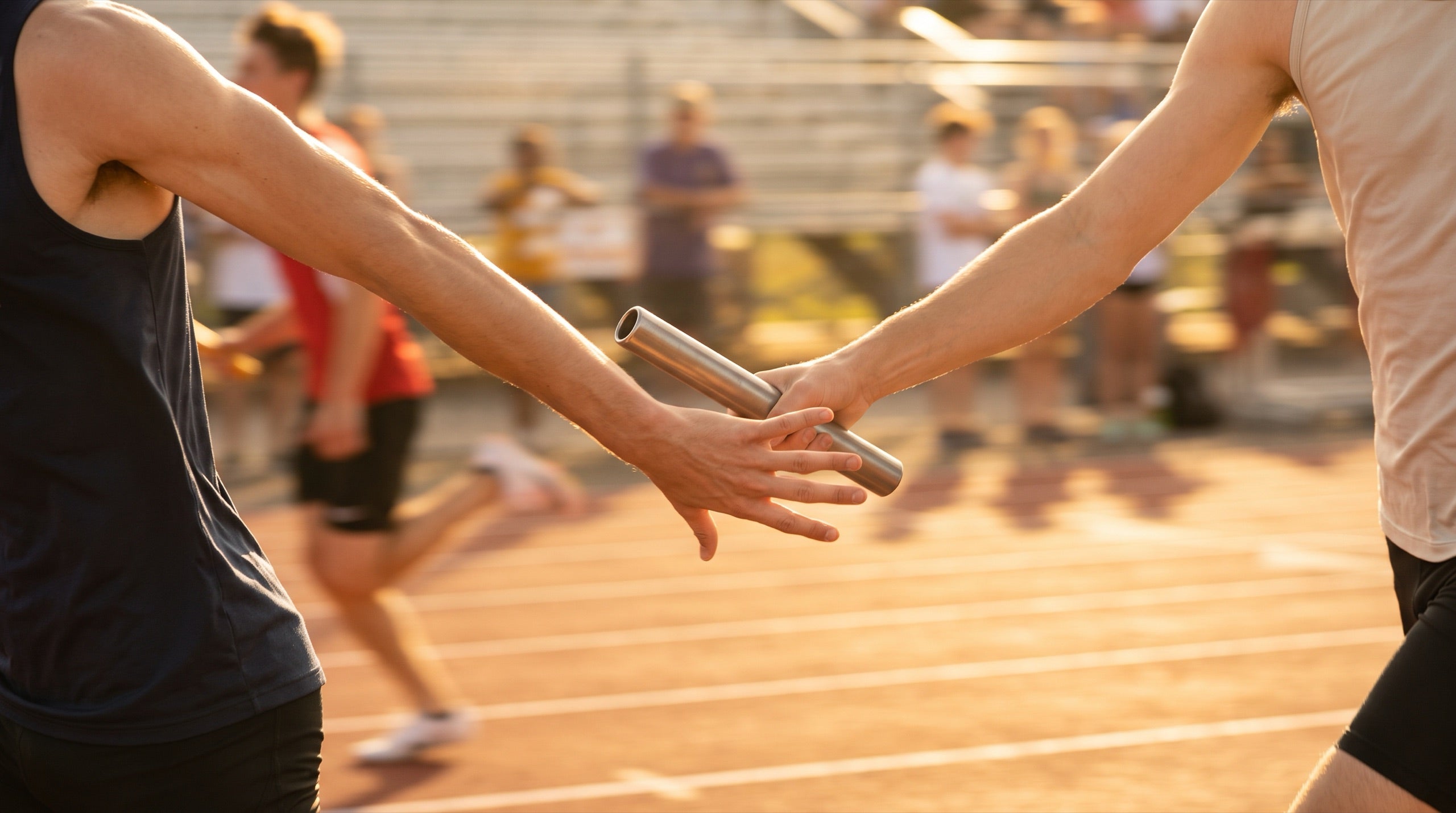 Close-up of a relay baton passing between two runners' hands at golden hour
